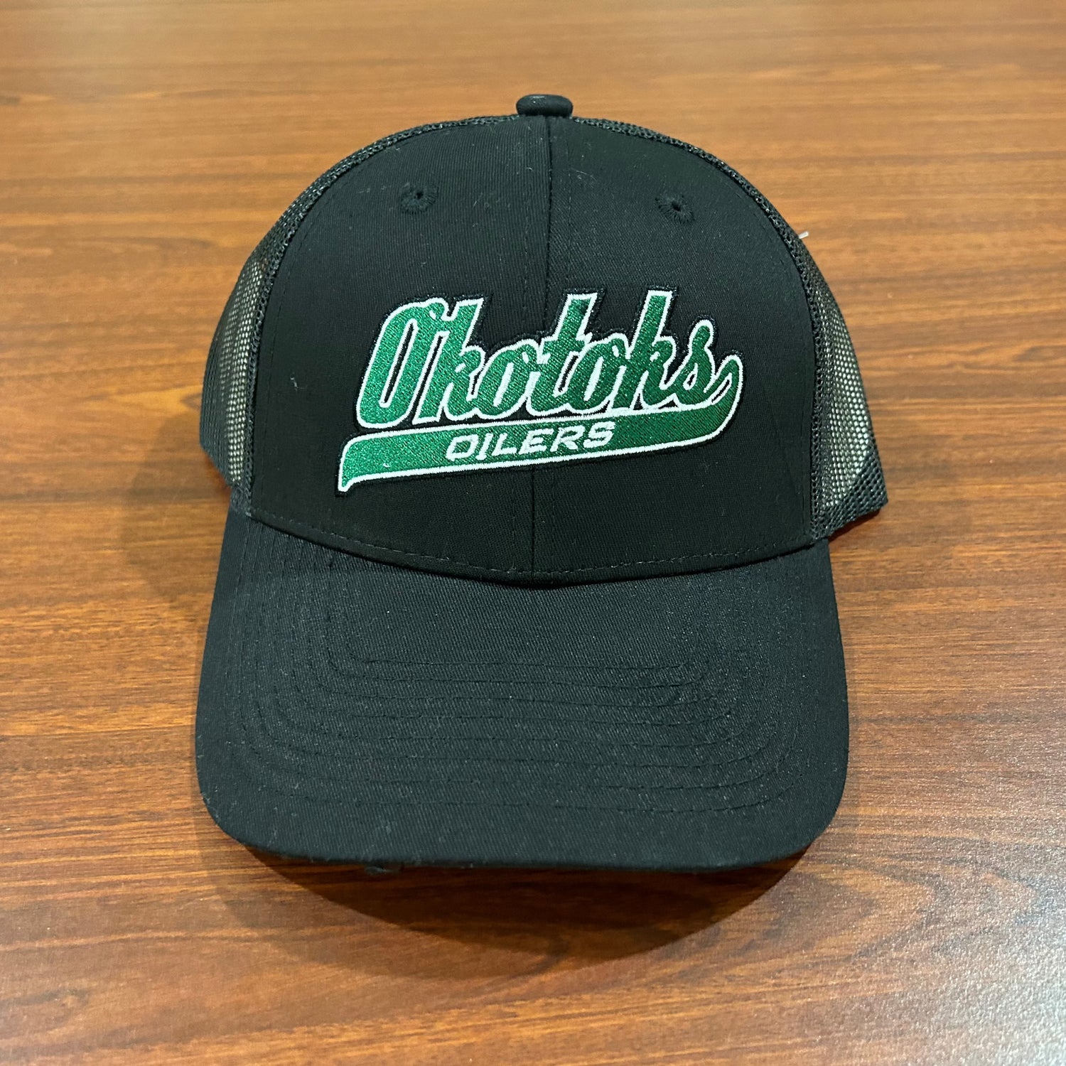 Front view of a black baseball cap featuring the Okotoks Oilers' green script logo.