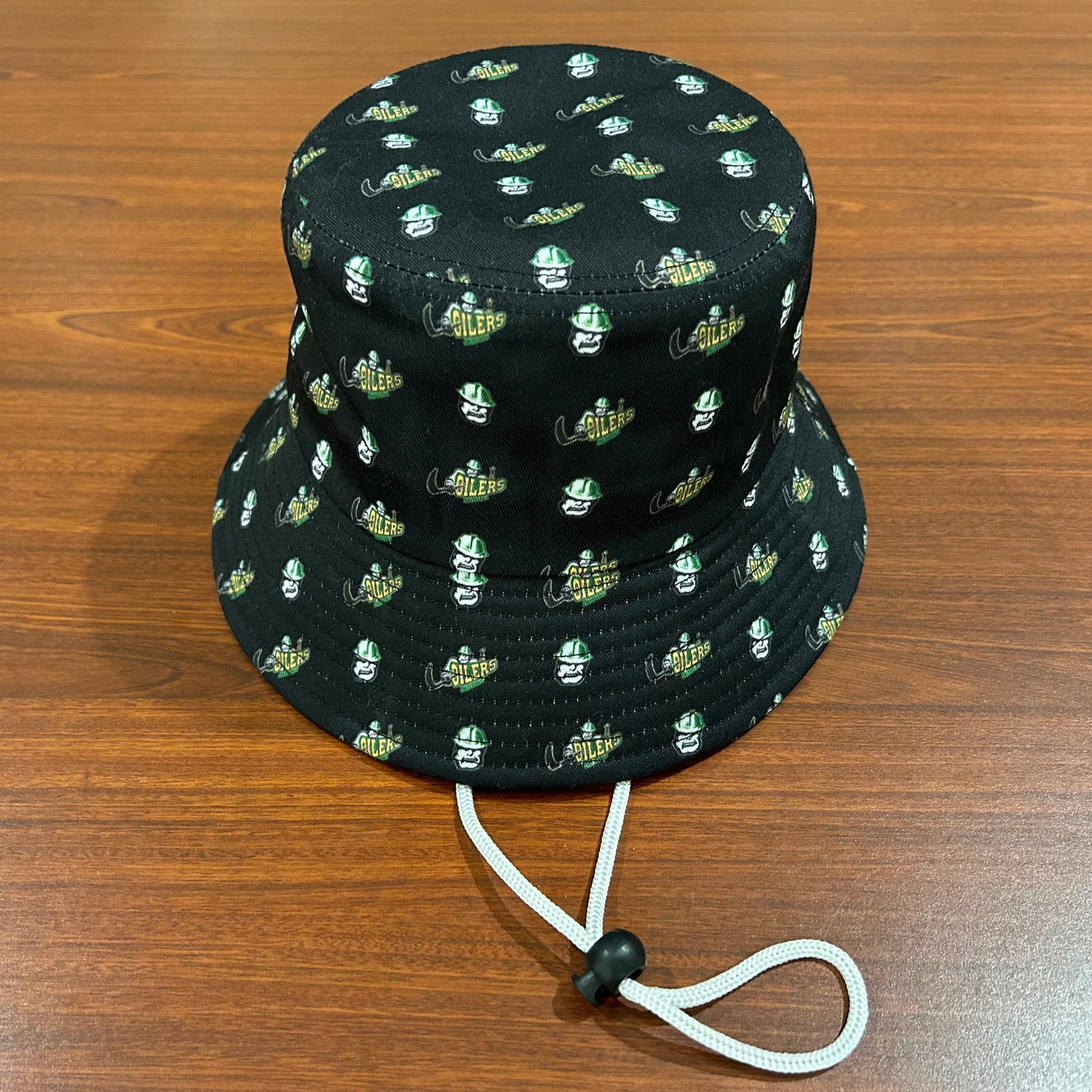 Black bucket hat with a pattern of minature Oilers Rigger head and primary logos. The hat also has a white drawstring.