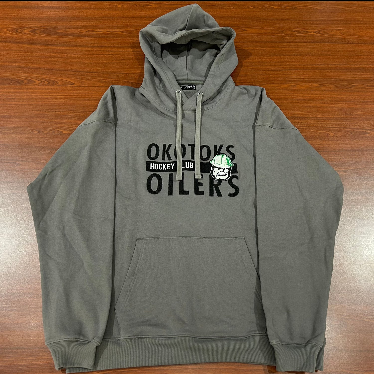 Grey hoodie with OKOTOKS OILERS HOCKEY CLUB and the Okotoks Oilers' Rigger head logo embroidered on the chest. The hoodie also has a grey drawstring.